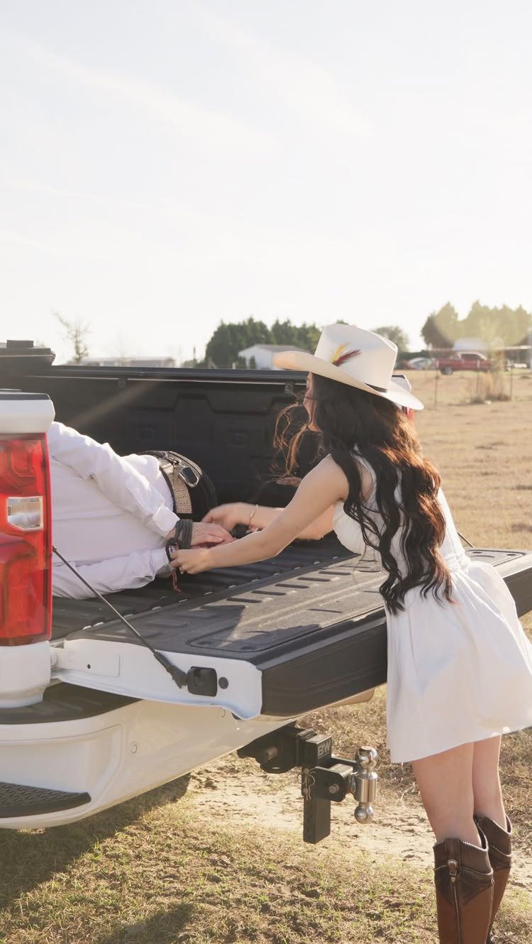Woman in white dress and cowboy hat reaching for man in pickup truck