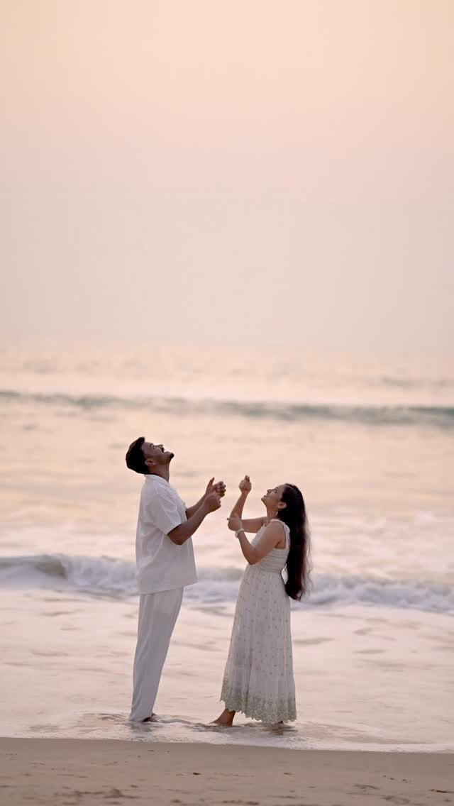 Couple in white clothing standing on a beach looking up at the sky.