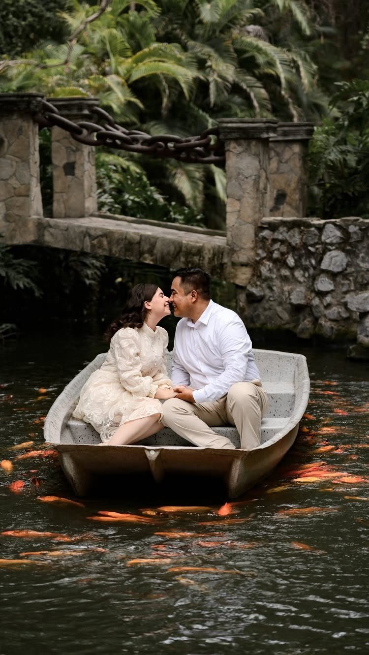 Couple in a white boat on a koi pond with a stone bridge background
