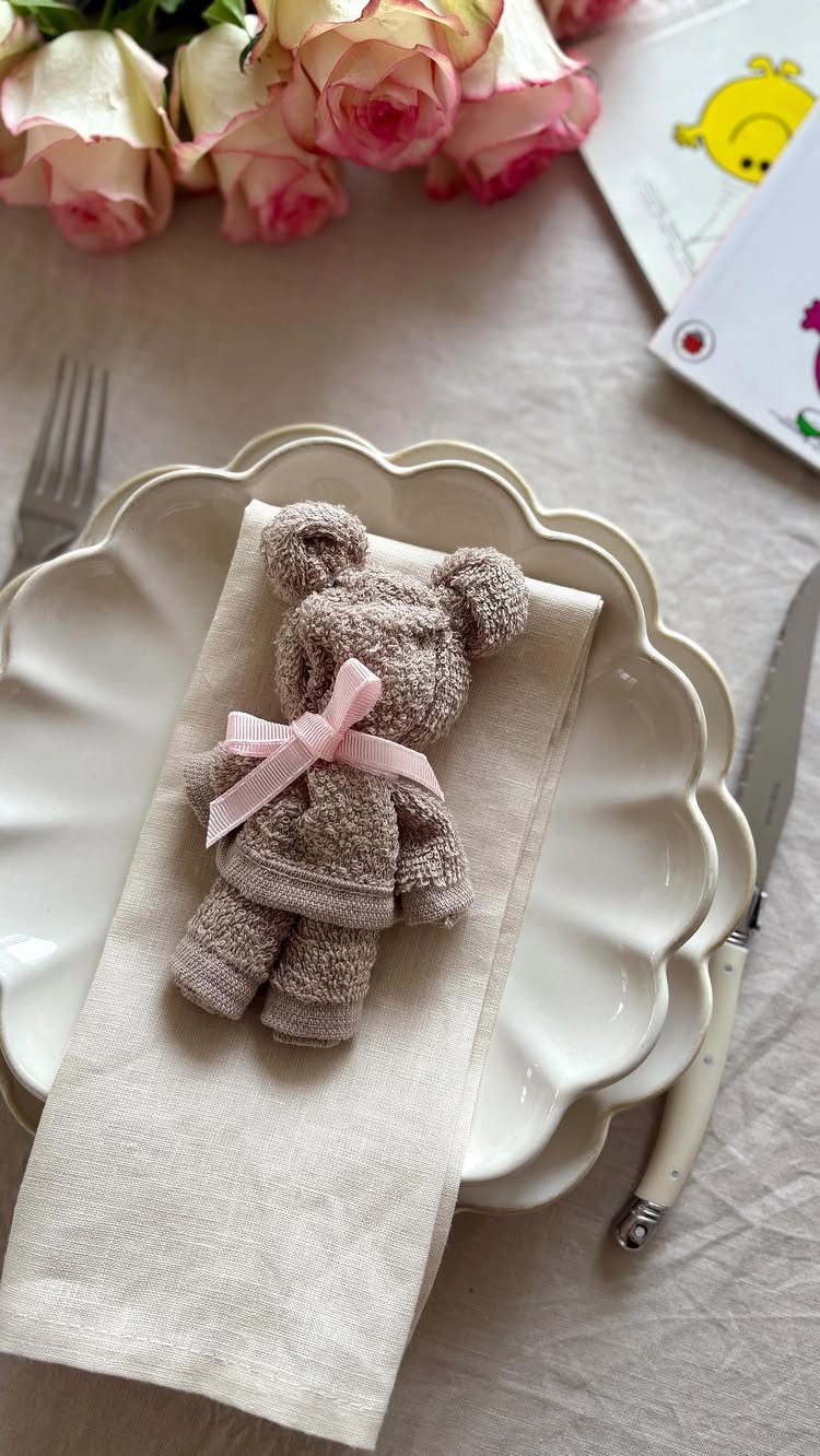 Towel bear with pink ribbon on a beige napkin and white scalloped plates.