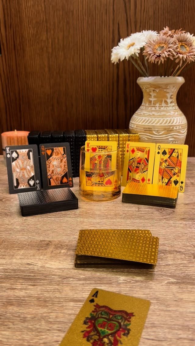 Playing cards in black and gold arranged on a wooden table with flowers.