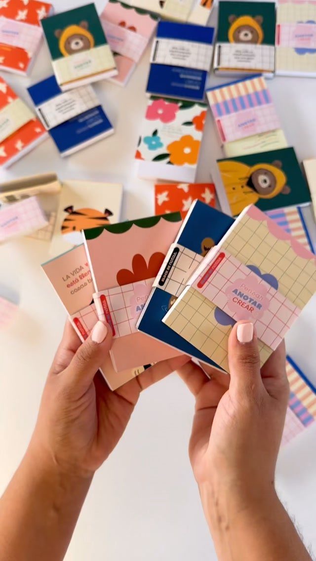 Hands holding a variety of colorful mini notebooks with cute illustrations and patterns.