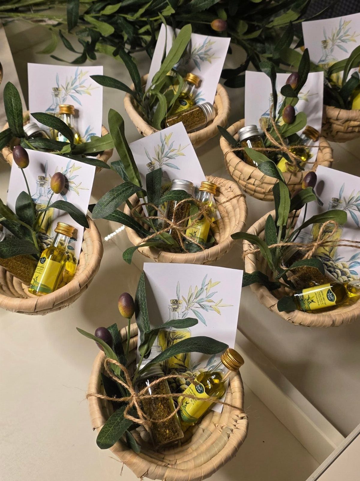Mini olive oil bottles in small woven baskets with olive leaves and cards.