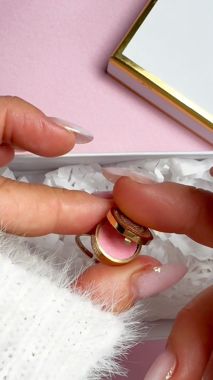 Small gold compact with pink interior held over white shredded paper in box
