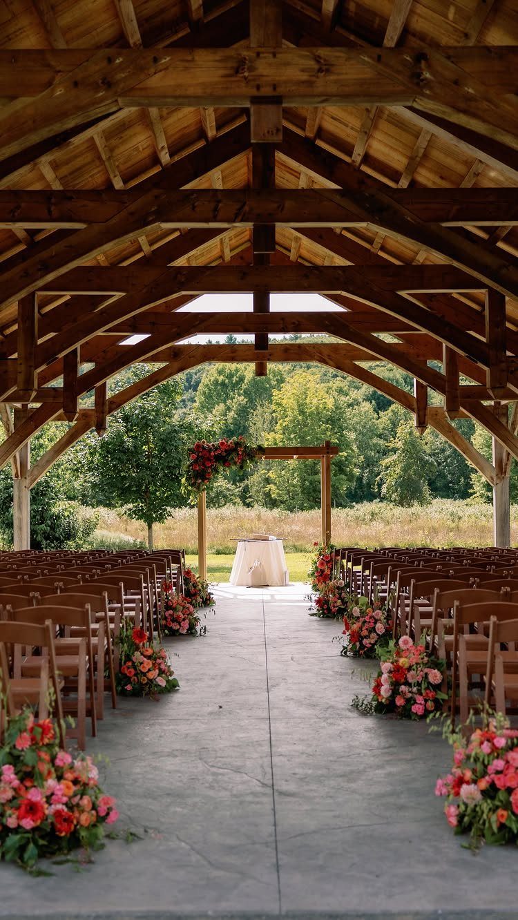 Wedding ceremony setup under a rustic wooden pavilion with floral aisle decorations.