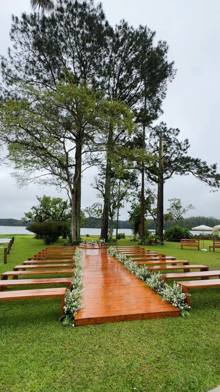 Wooden wedding aisle and benches on a grassy lawn beside a calm lake.