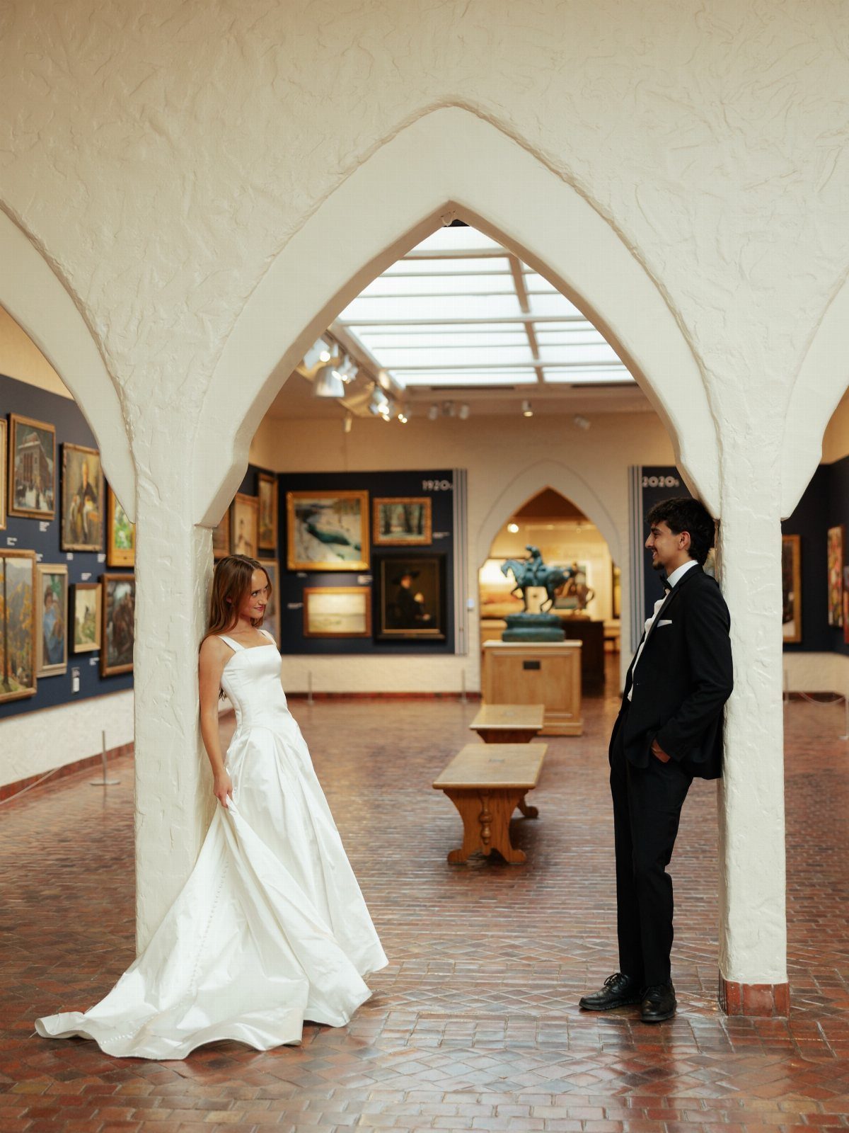 Bride and groom posing in an art museum gallery framed by a white arch.