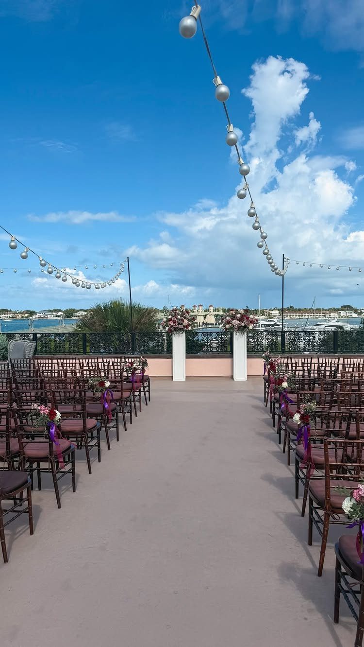 Rooftop wedding ceremony setup with brown chairs, floral altar, and overhead string lights.