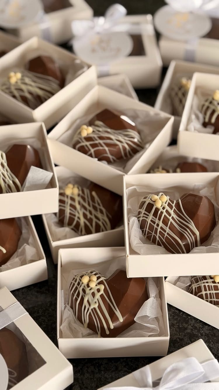 Heart-shaped chocolates with white drizzle in small white gift boxes for wedding favors.