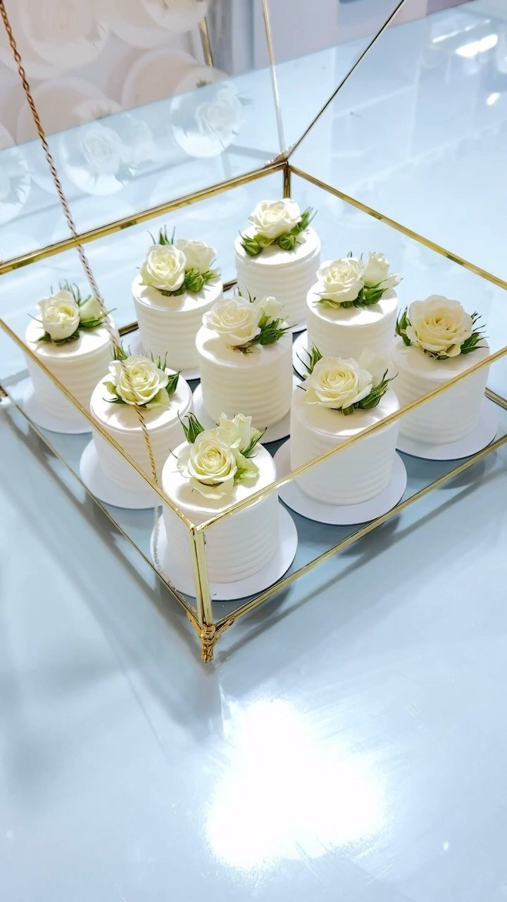 Small white frosted cakes with roses inside a gold glass display box