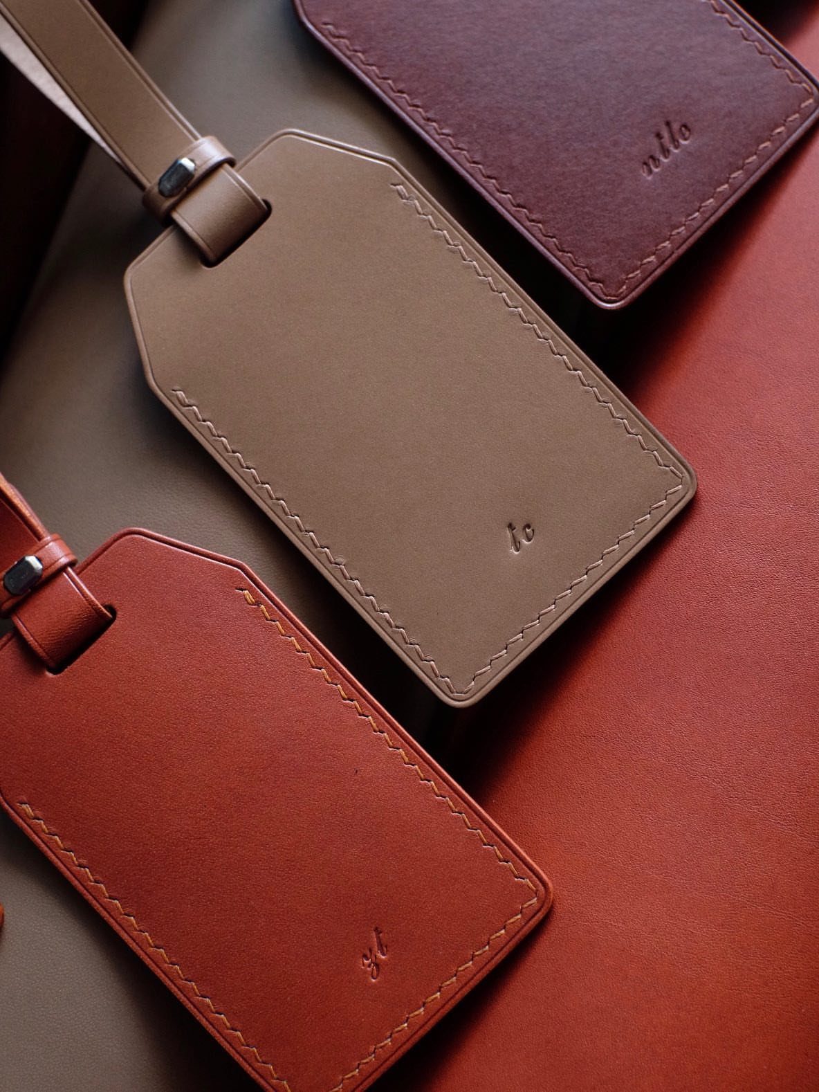 Leather luggage tags in burgundy, tan, and brown with embossed initials.