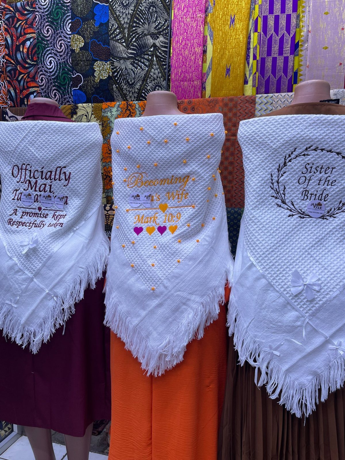 Three personalized white fringed shawls with wedding embroidery displayed on mannequins.