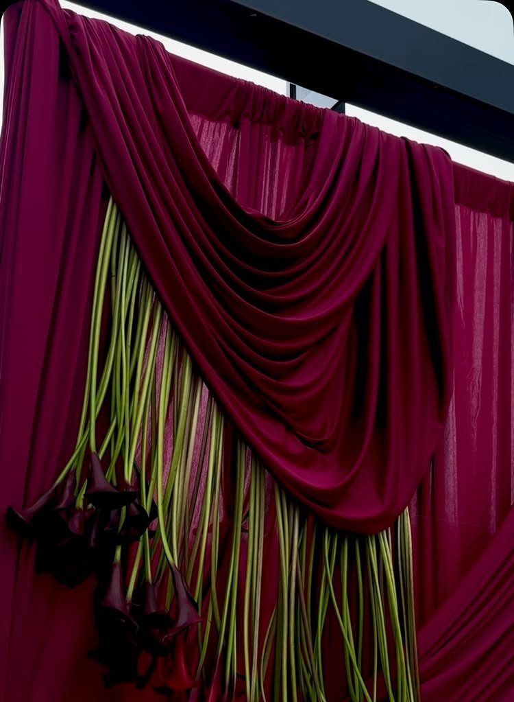 Magenta draped fabric backdrop with green accents and purple calla lilies.