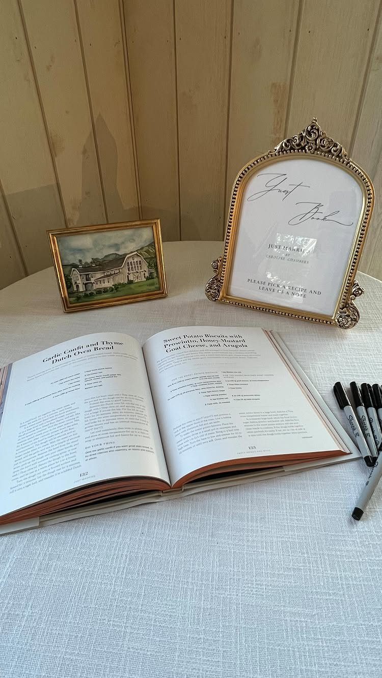 Open guestbook on a white table with black markers and gold frames.