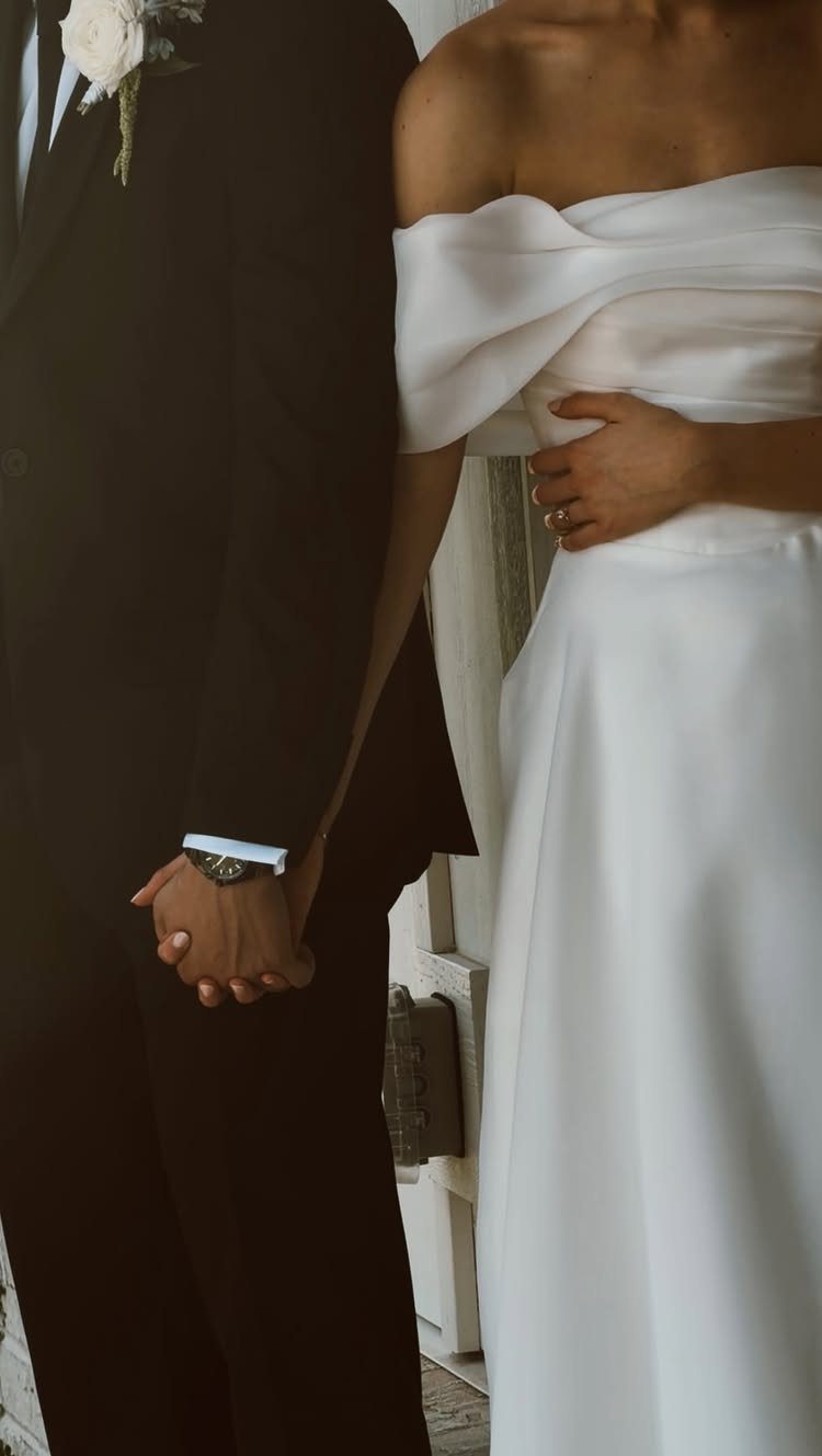 Couple in wedding attire holding hands, featuring a black tuxedo and white gown.