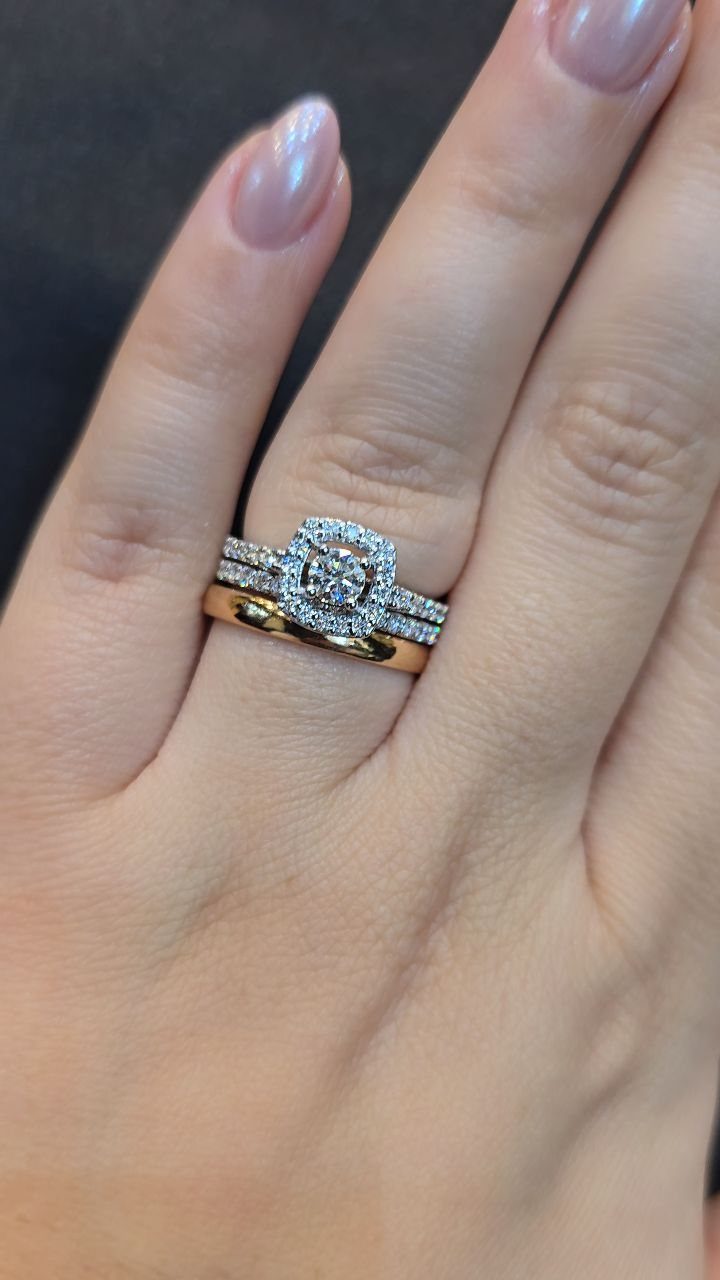 Three stacked wedding and engagement rings on a finger with shimmering pink nails.