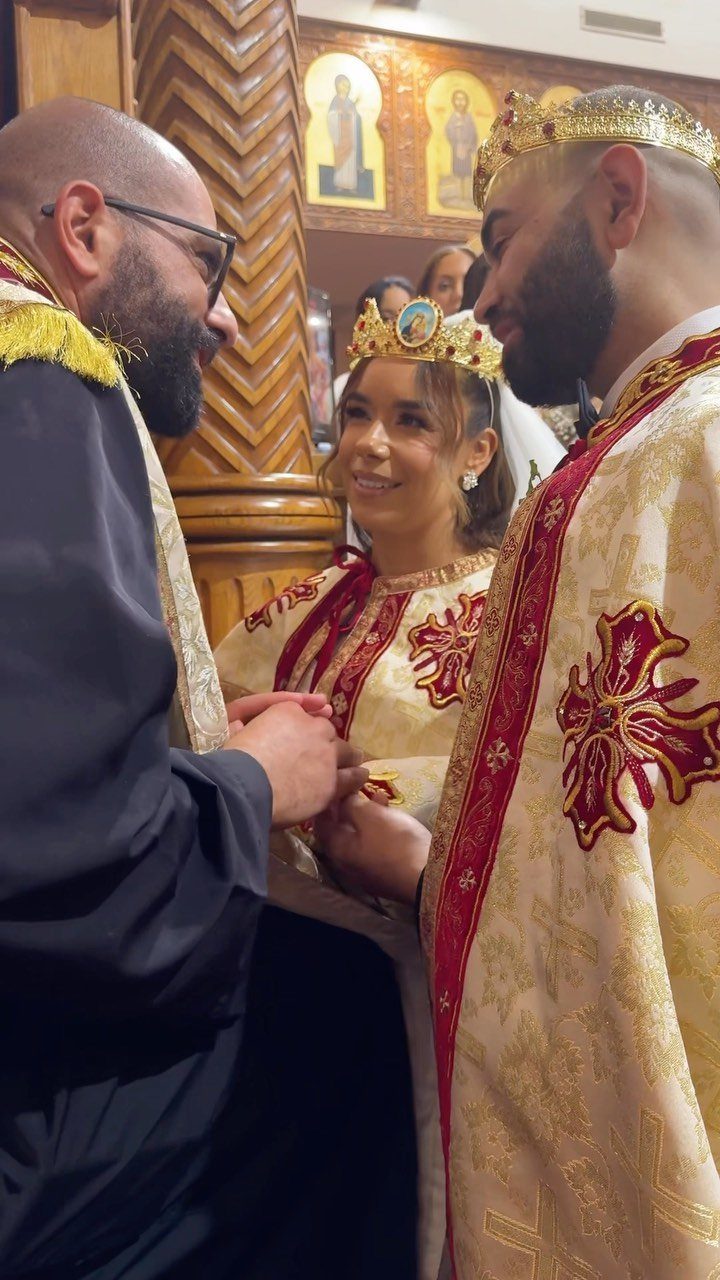 Couple wearing gold crowns and ceremonial robes during a wedding crowning ritual.