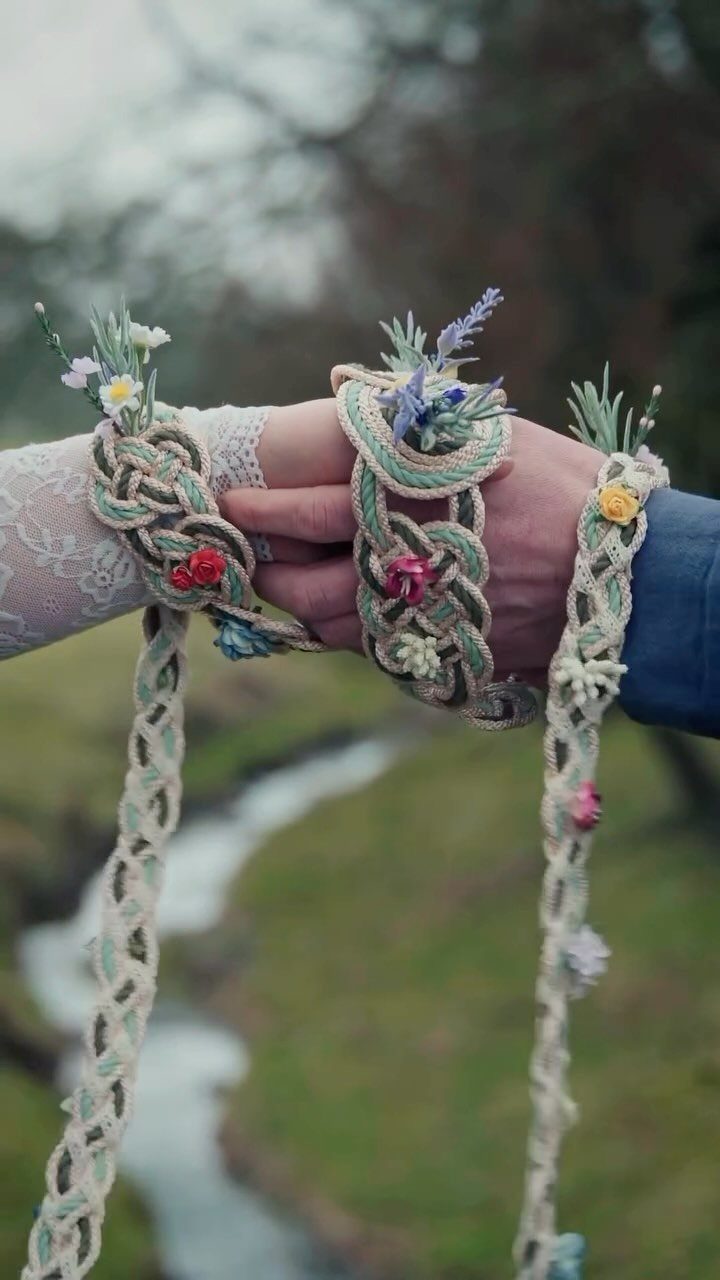 Hands of a couple bound together with a braided floral cord outdoors.