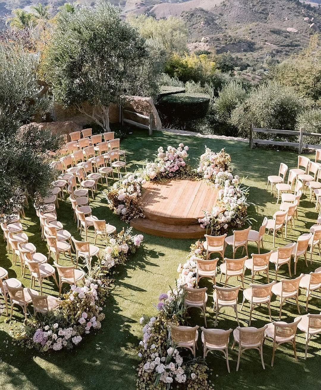 Circular wooden wedding platform surrounded by flowers and chairs on a grassy hillside.