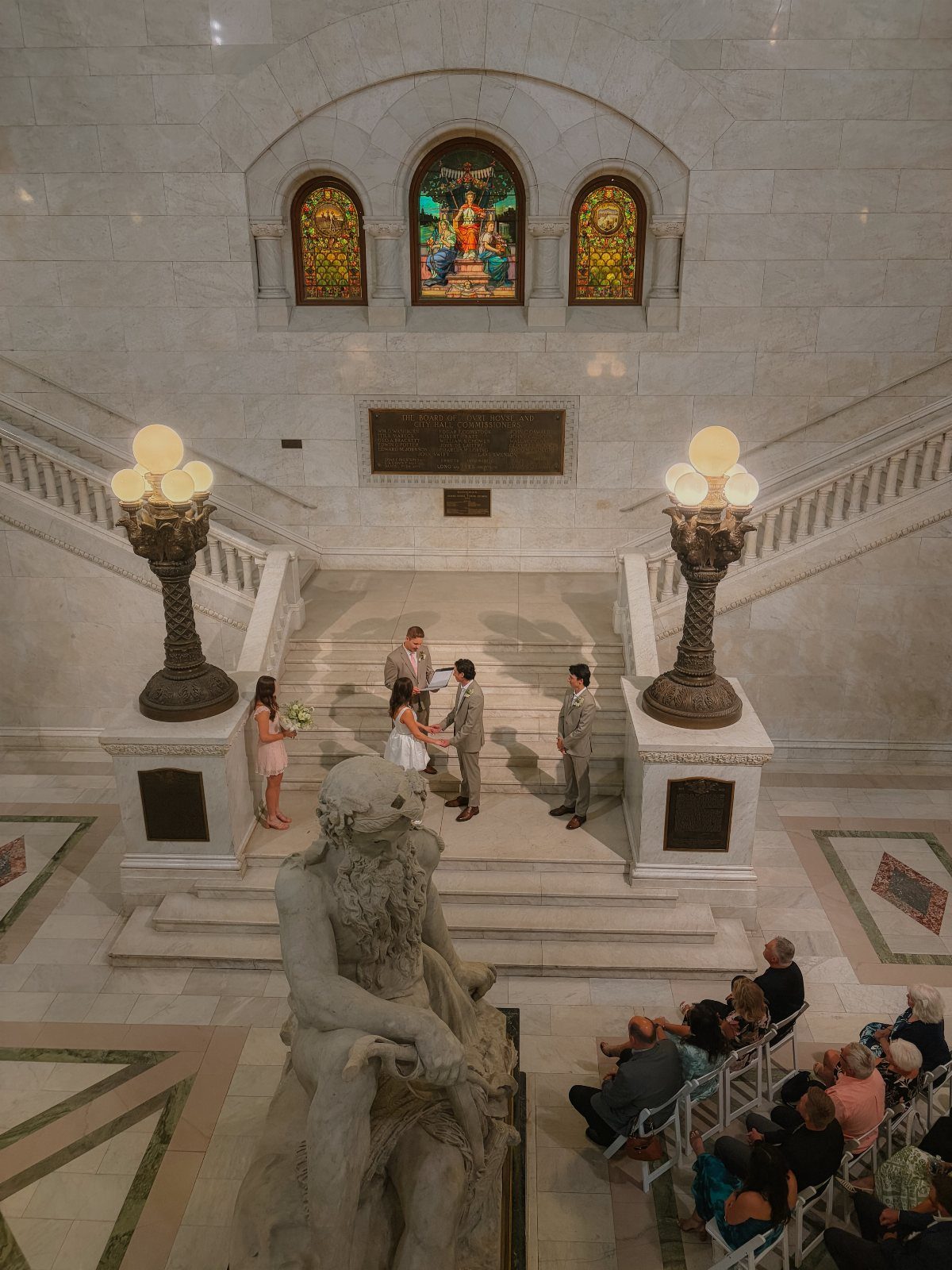 Wedding ceremony on white marble stairs in a grand hall with stained glass.