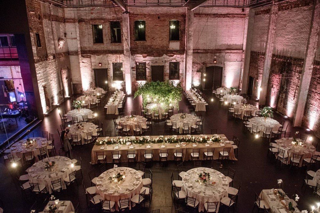 Industrial event space with exposed brick walls and white clothed wedding reception tables.