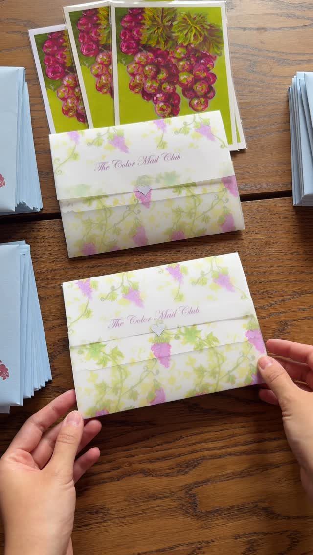 Translucent vellum envelopes with floral prints and grape-themed cards on a wooden surface.