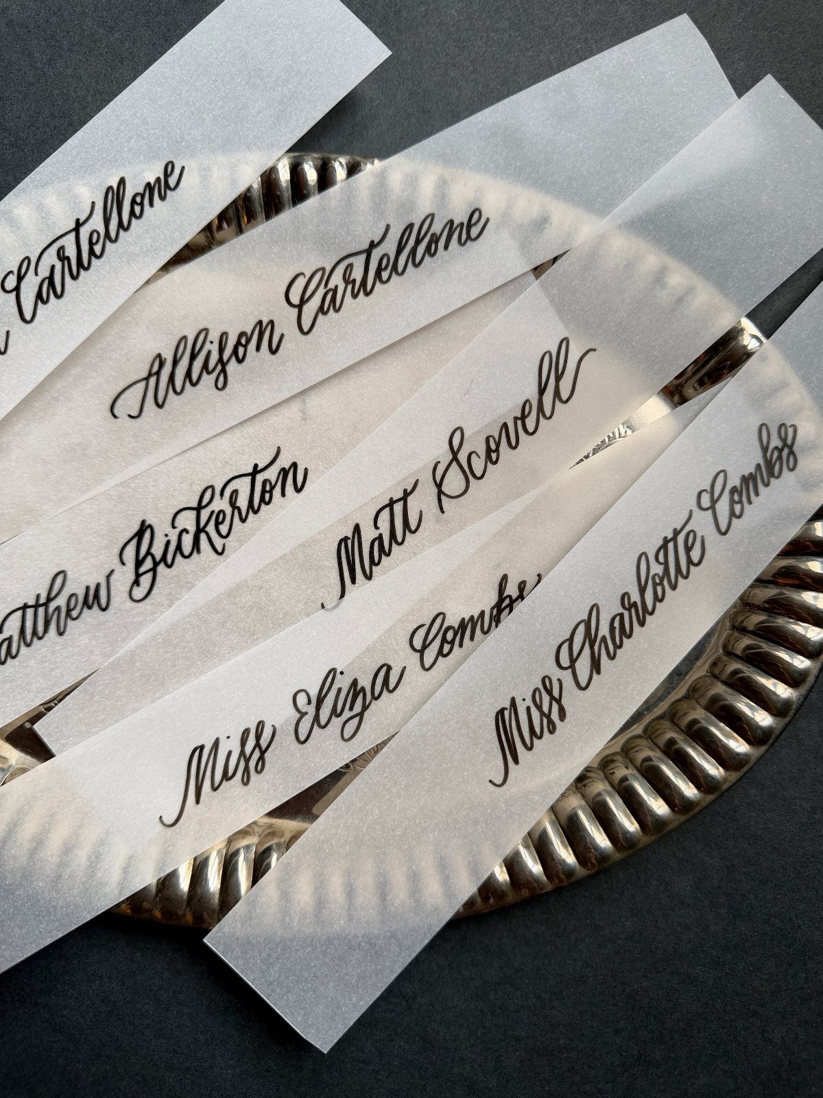 Translucent vellum paper strips with black calligraphy resting on a silver platter