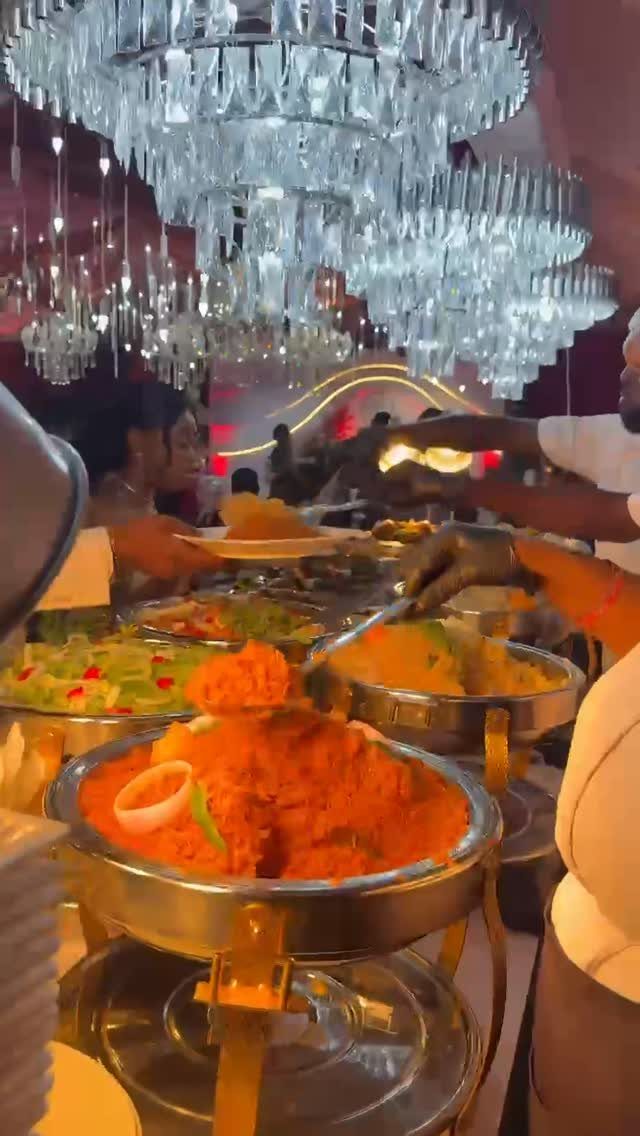 Buffet food in silver chafing dishes under a large crystal chandelier at a wedding.