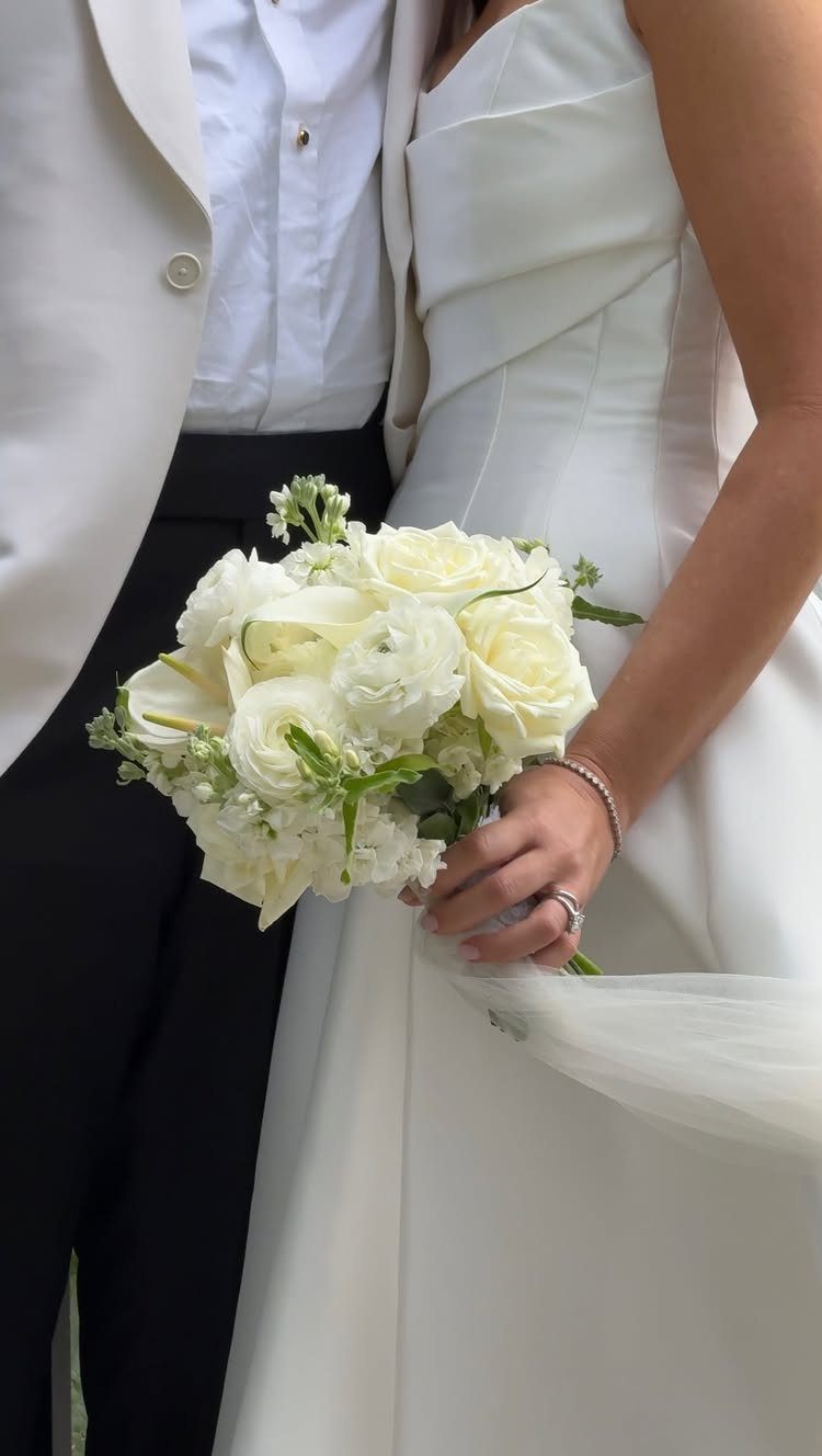 White bridal bouquet of roses and lilies held by a bride and groom.