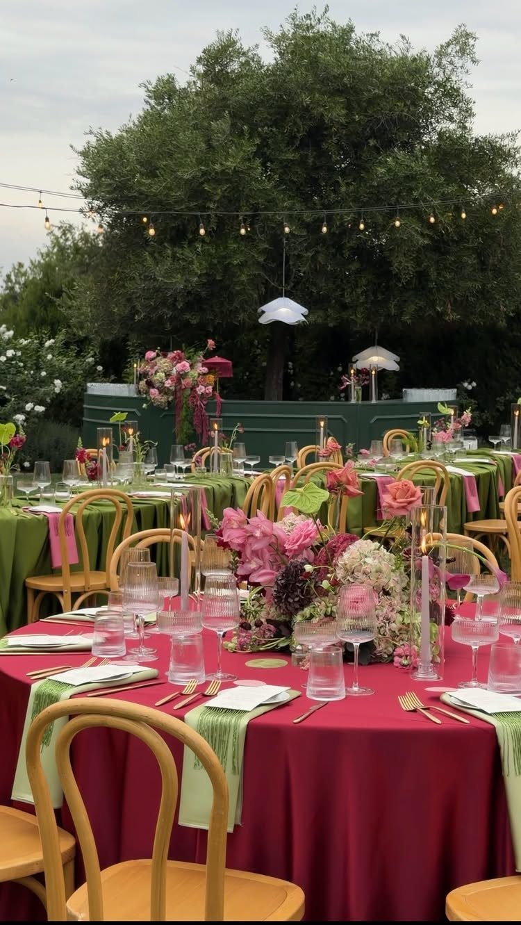 Outdoor wedding reception tables with red linens, pink flowers, and overhead string lights.