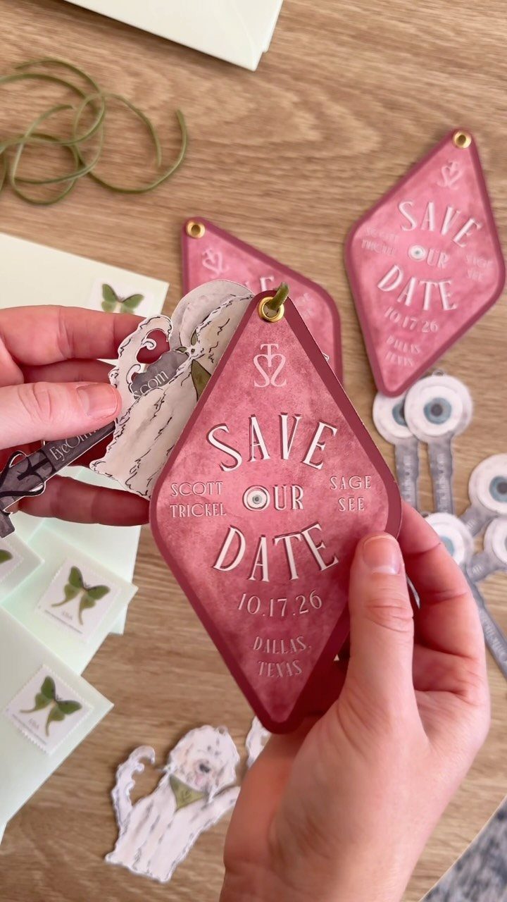 Diamond-shaped burgundy save the date card with Art Deco geometry held by hands.