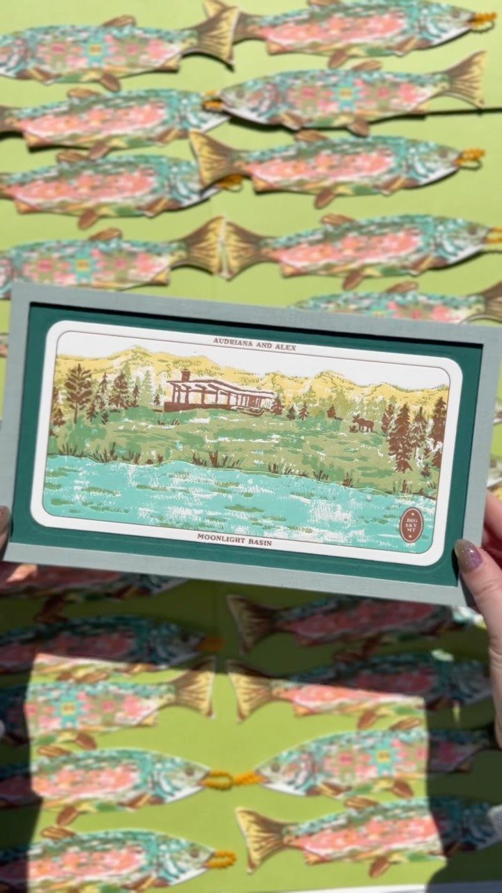 Illustrated postcard of a mountain lodge held above colorful fish-shaped paper cutouts.
