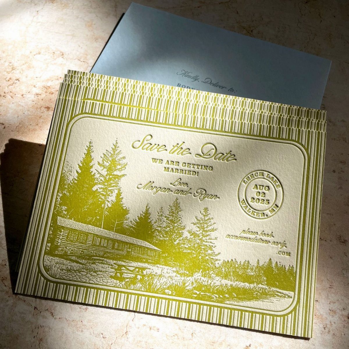 Gold save-the-date card with a rustic log cabin illustration and vintage postmark stamp.