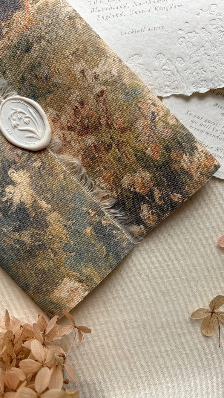 Floral fabric invitation folder with a white wax seal and deckle-edged paper.