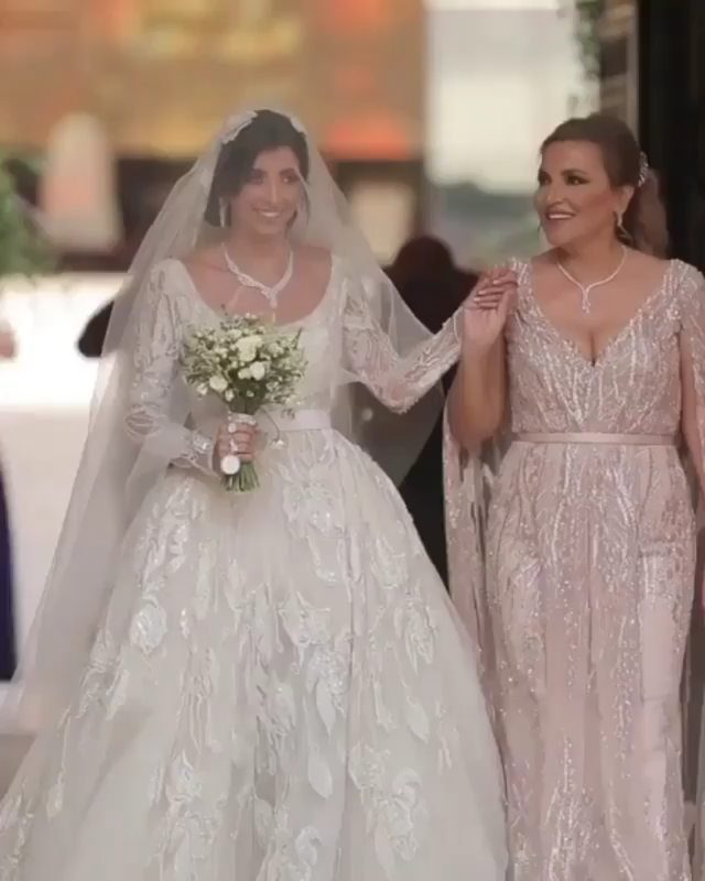 Bride in white lace gown walking arm-in-arm with a woman in pink.