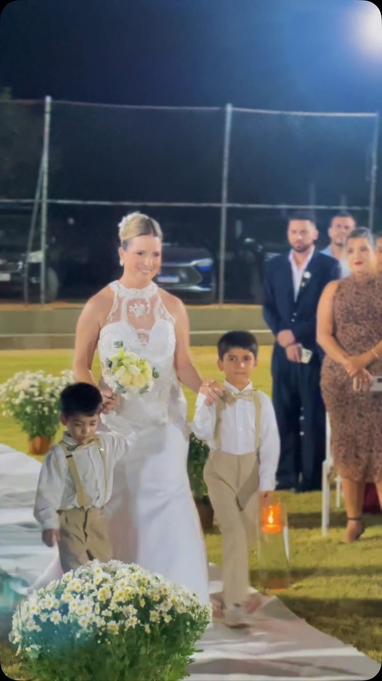 Bride in white lace dress walking down the aisle with two young boys.