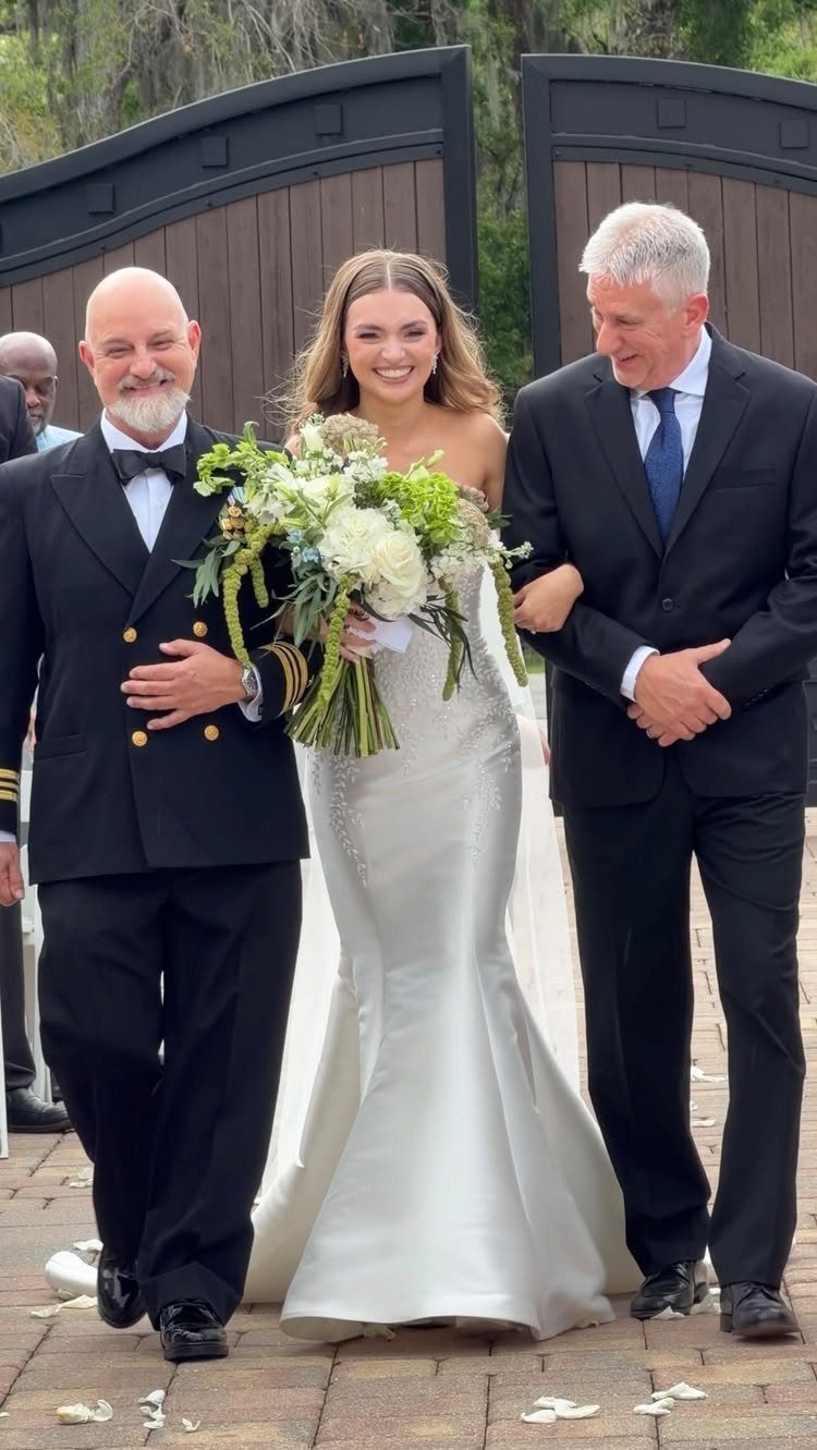 Bride in white gown walking down the aisle with two men in suits.