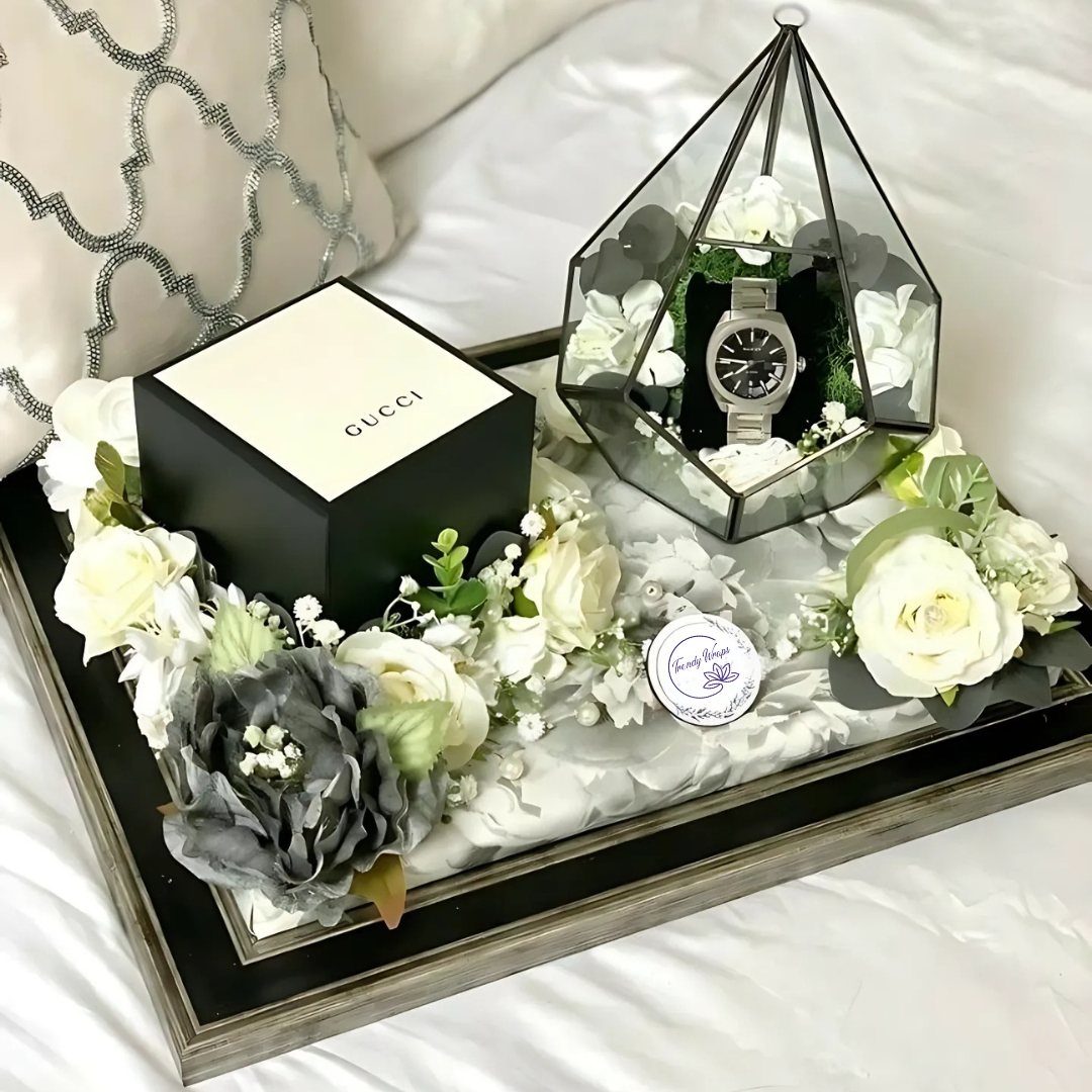 Wooden tray with Gucci box, watch in glass terrarium, and white roses.