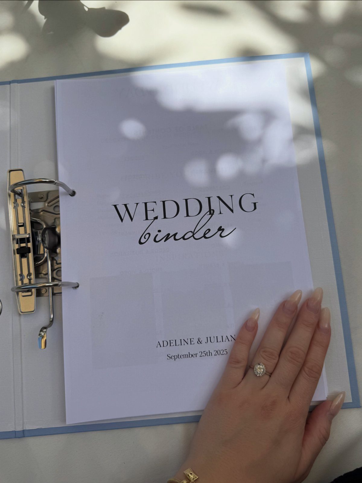 Wedding binder with names and date, held by a hand with a ring.