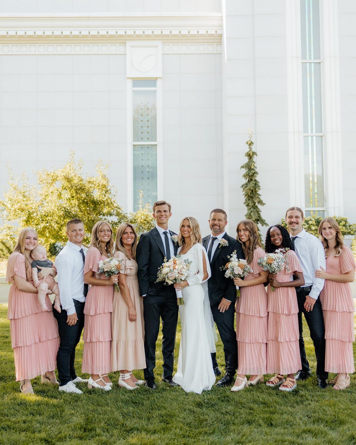 Wedding party posing on a lawn with a bride, groom, and attendants.