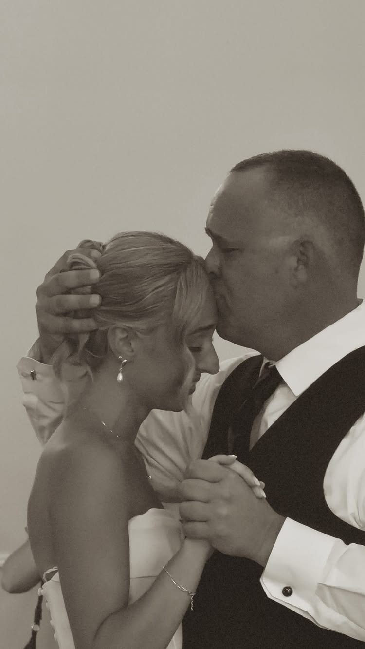 Man in a vest kissing a bride on the forehead during a dance.
