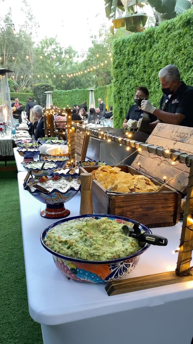 Taco bar with guacamole, salsa, and tortilla chips served outdoors at a wedding.