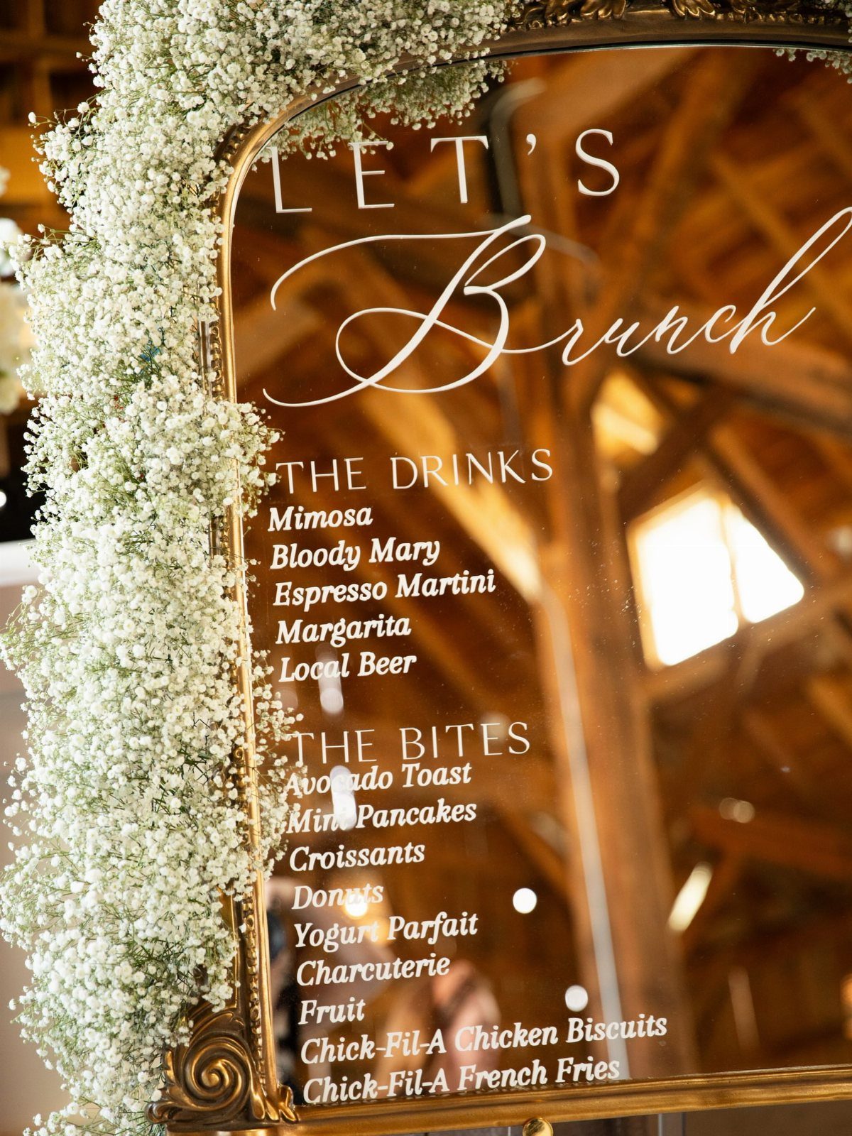 Gold-framed mirror menu listing brunch drinks and bites decorated with white baby's breath.