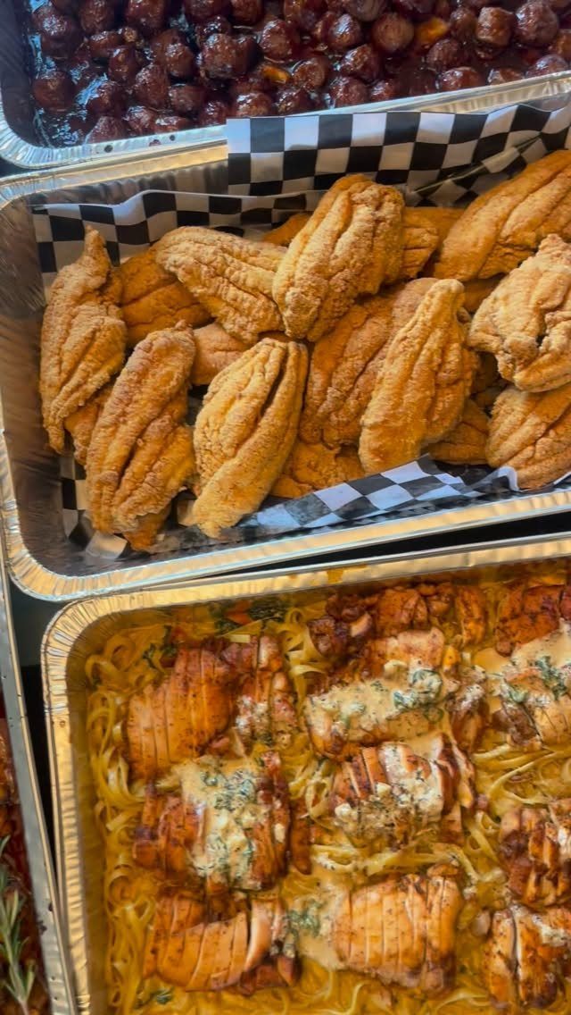 Aluminum catering trays filled with fried fish, chicken pasta, and glazed meatballs.