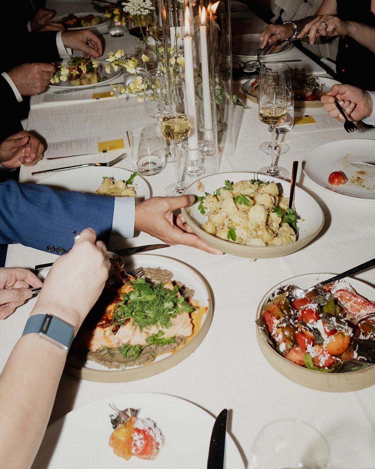 Shared platters of salmon and vegetables on a white tablecloth dinner table.