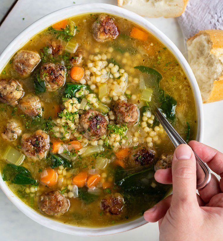 Meatball soup with pasta and vegetables in a white bowl with crusty bread.