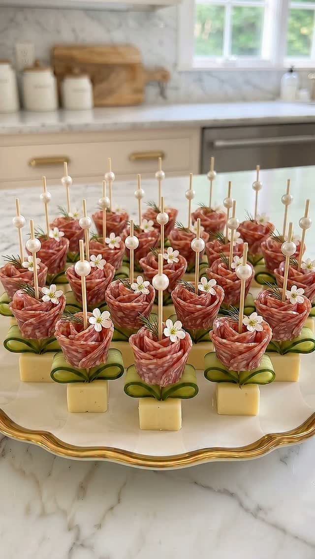 Salami roses on cheese and cucumber cubes arranged on a gold-rimmed white platter.