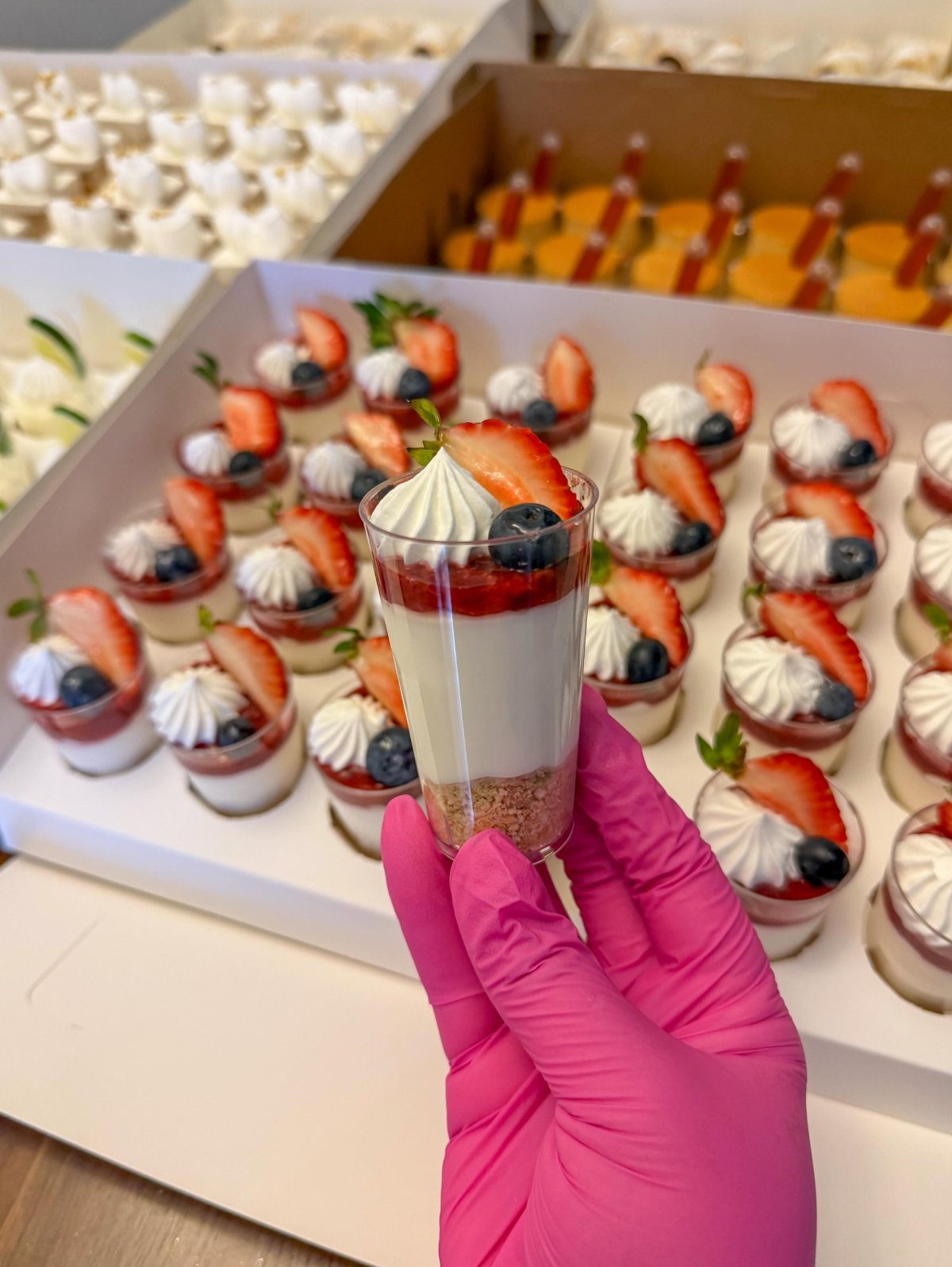 Layered mini dessert in a plastic cup with strawberry and blueberry toppings.
