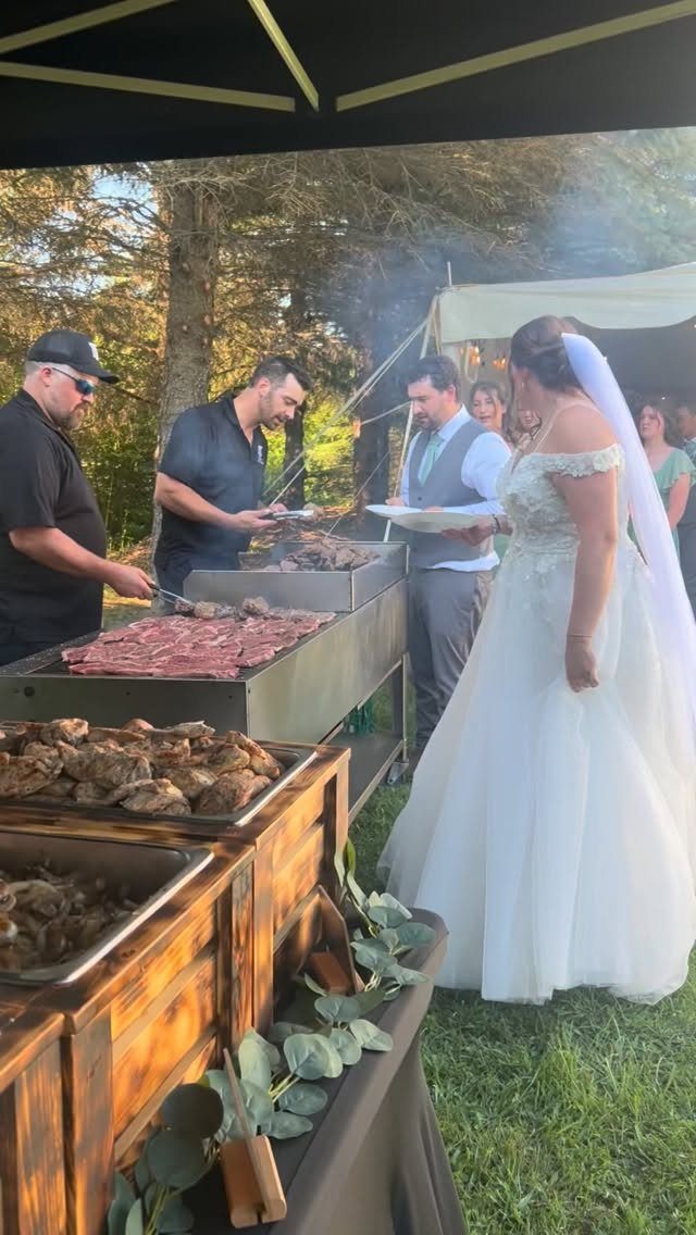 Bride and groom at an outdoor wedding buffet with chefs grilling meat.
