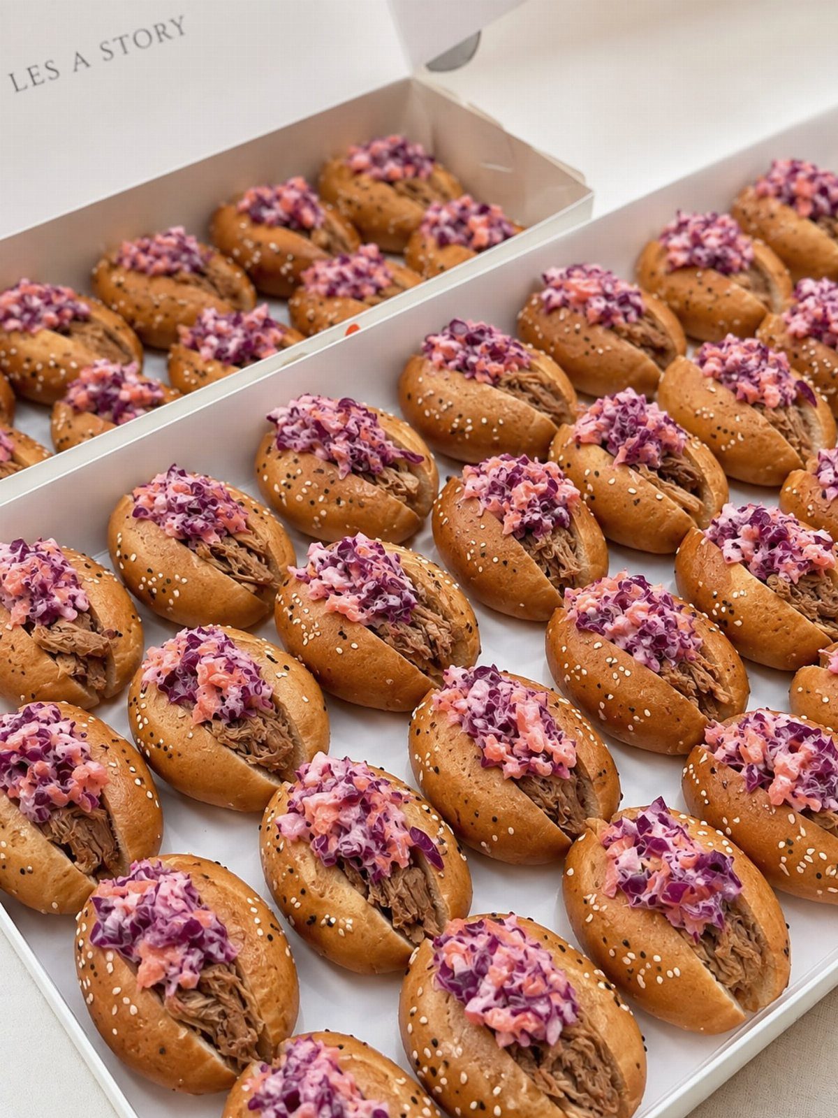Pulled pork sliders with purple coleslaw in white catering boxes.